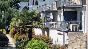 Un edifici de diverses plantes amb balcons, seients a l'exterior i una palmera.