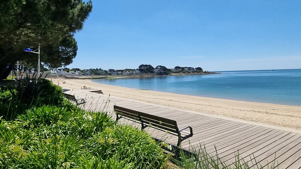 Una platja amb un passeig marítim de fusta, bancs i vegetació.
