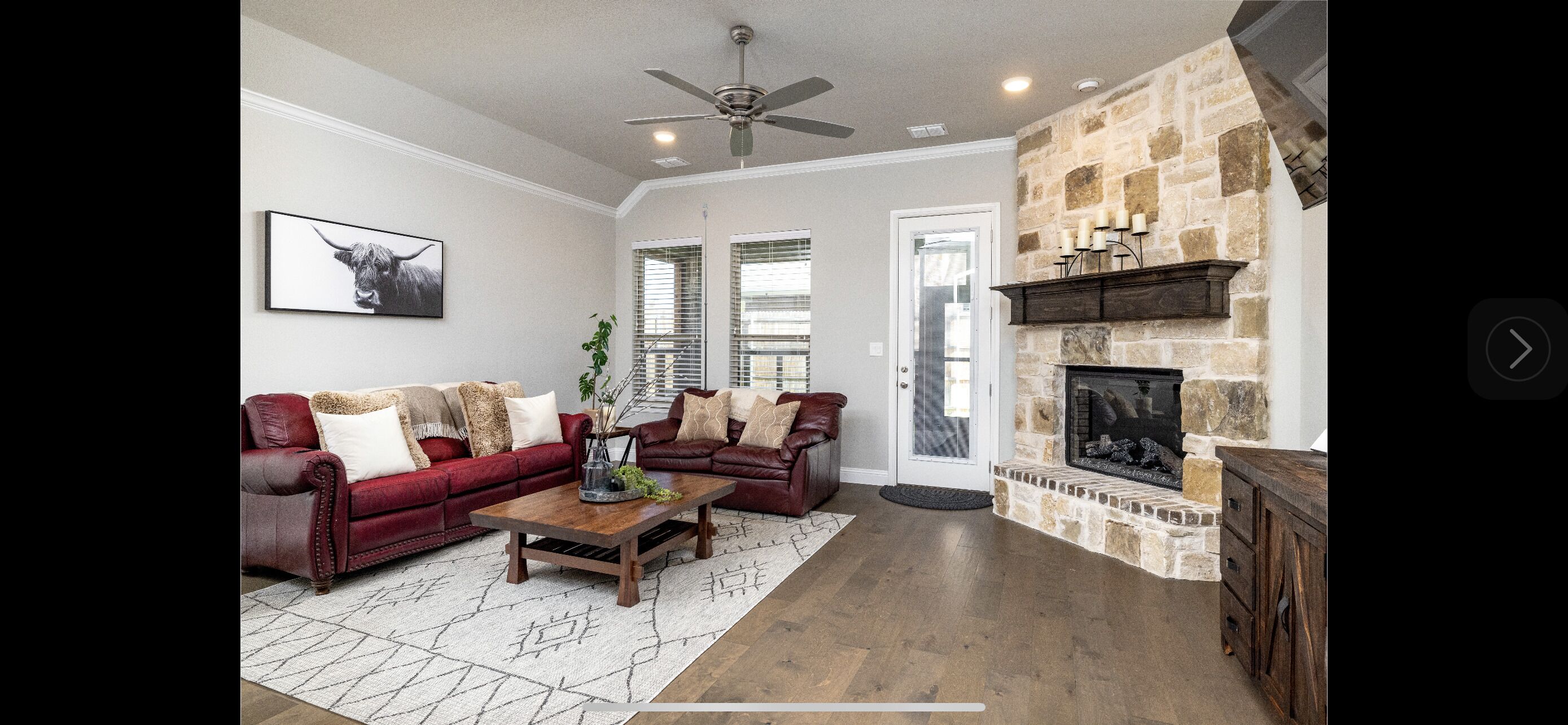 A living room with a stone fireplace, leather sofas, and a ceiling fan.