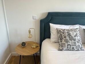 Ein ordentlich eingerichtetes Schlafzimmer mit einem Bett, einem Nachttisch mit Lampe und einem an der Wand montierten Lichtschalter.