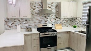 Una cocina moderna con armarios de madera clara, estufa negra, electrodomésticos de acero inoxidable y un salpicadero con diseño.