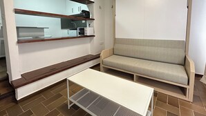 Un espacio habitable compacto con kitchenette, sofá y una pequeña mesa.
