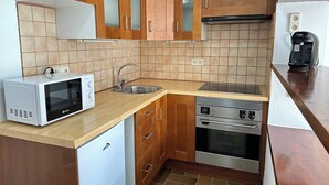 A compact kitchen with wooden cabinets, a stainless steel sink, a microwave, and a built-in oven. - Agi Porthos 113 Apartamento for rent in Roses Girona. (Roses)