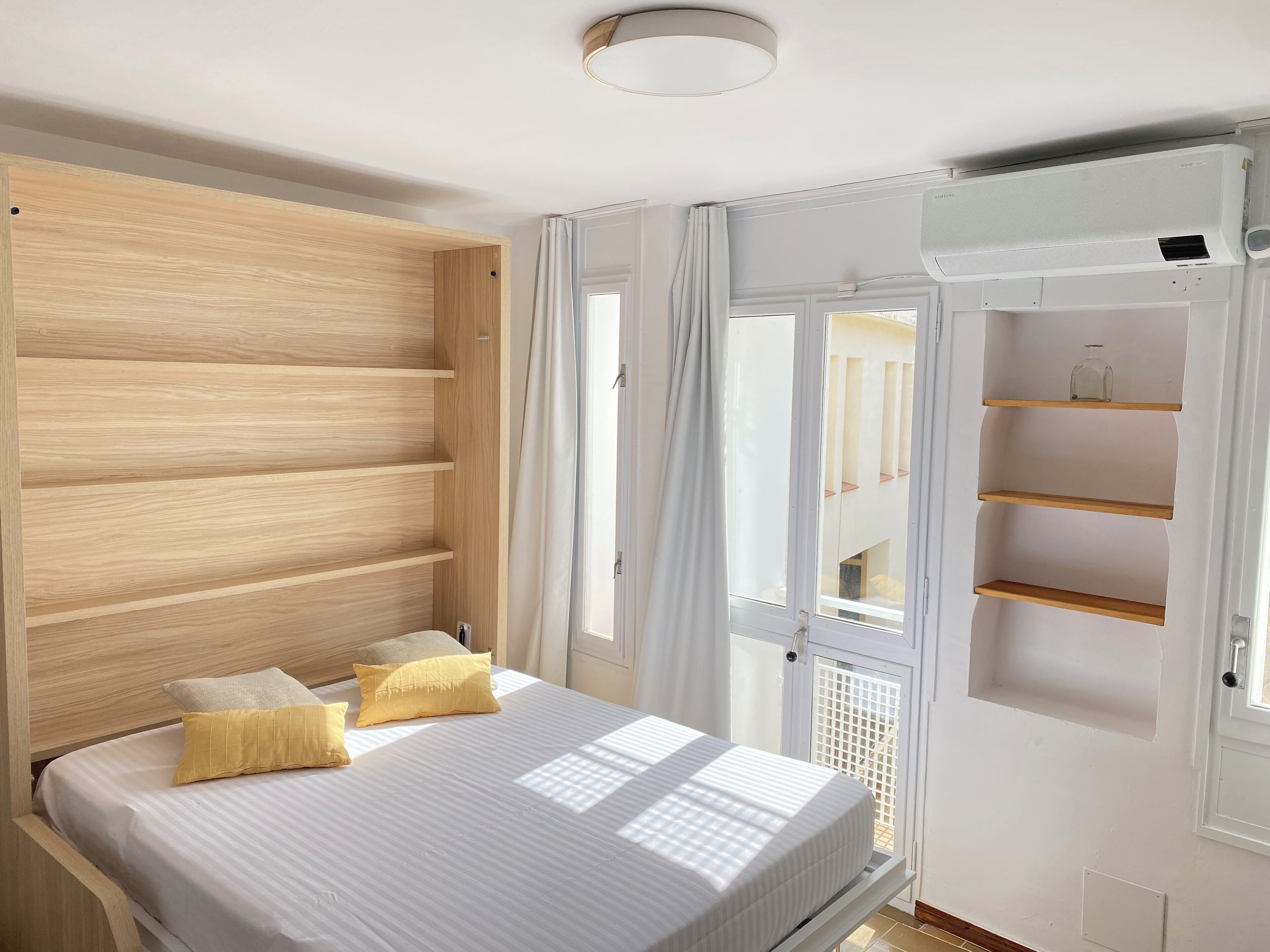 A bedroom with a wooden headboard, a bed with white bedding, and a window with a view of the outside.