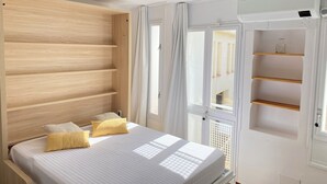 A bedroom with a wooden headboard, a bed with white bedding, and a window with a view of the outside. - Agi Porthos 113 Apartamento for rent in Roses Girona. (Roses)