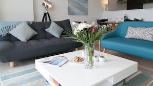 A modern living room with a dark grey sofa, a blue sofa, and a white coffee table with a vase of flowers and a magazine.