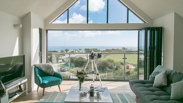 A spacious living room with a large bay window offering a view of the sea and a telescope on a tripod.