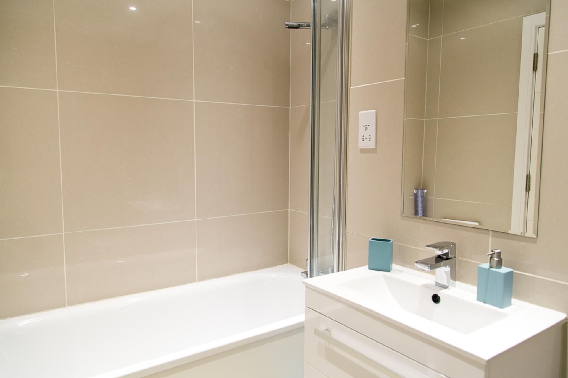 A modern bathroom with a bathtub, a glass shower enclosure, a white vanity with a mirror, and a blue soap dispenser.