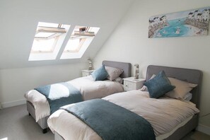 A bedroom with two beds, a skylight, and a painting of a coastal scene.
