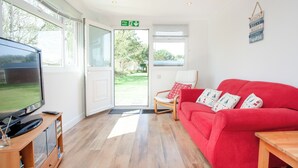 A room with a television, a red sofa, a wooden table, a rocking chair, and a door leading outside.