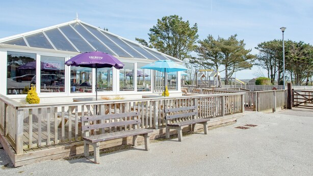 A wooden structure with a glass roof, benches, and umbrellas.