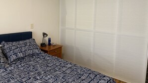 A bedroom with a bed, a nightstand, a lamp, and a window with blinds.
