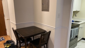 A small kitchen with a dining table and chairs, a wooden floor, and a white wall.