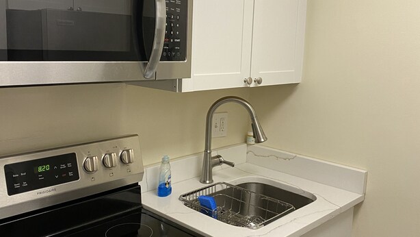 A kitchen with a stainless steel microwave, a digital clock, a stove with four burners, and a sink with a faucet.