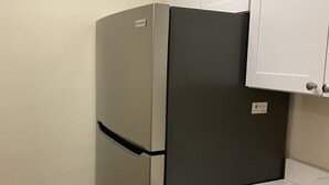 A compact kitchen with a built-in refrigerator, a white countertop, and a blue towel hanging on the door.