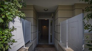 Un couloir étroit au sol en briques, bordé de murs blancs percés de plusieurs fenêtres ou panneaux.