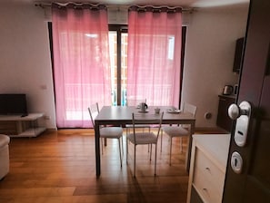 A room with a dining table, chairs, a TV on a shelf, and a door with a lock.