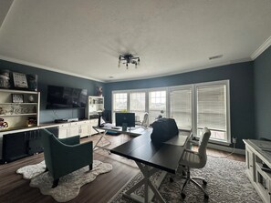 Un salon moderne doté d’un grand téléviseur à écran plat, d’un bureau avec un ordinateur et d’un coin salon confortable.