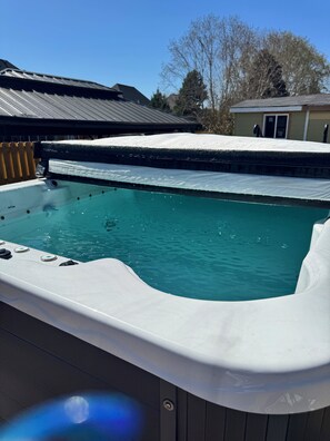 Un bain à remous avec une piscine à l’eau cristalline, entouré d’une terrasse en bois et surmonté d’une structure de toit en métal.