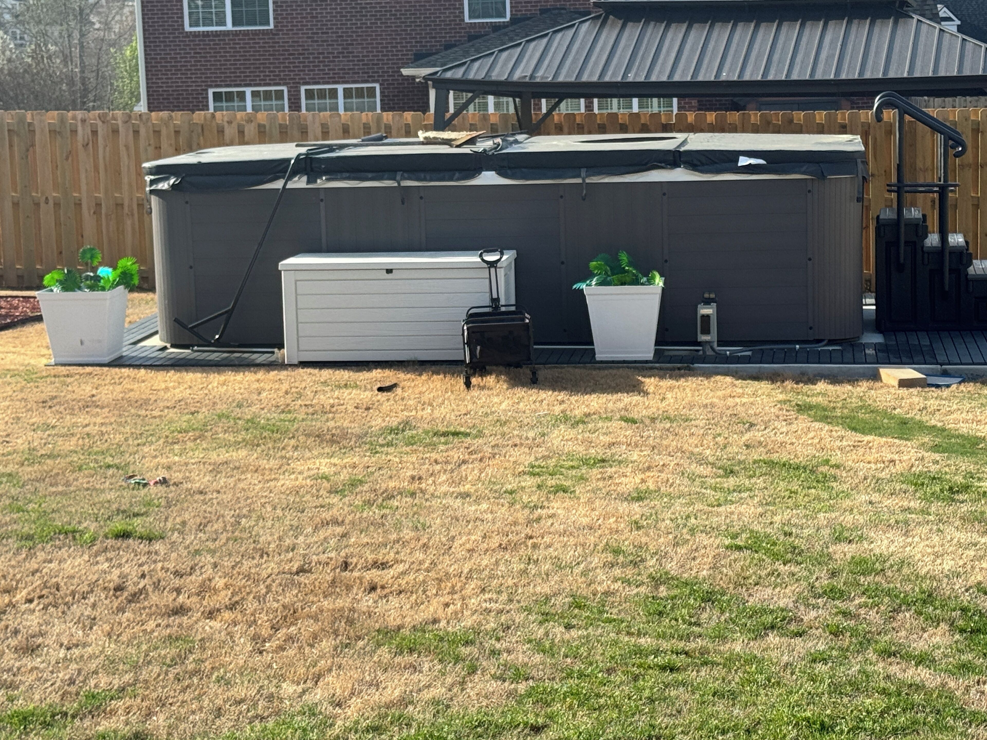 A backyard with a hot tub, a shed, and two planters with plants.