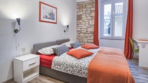 Een slaapkamer met een bed, nachtkastje, bureau, stenen muur en een raam met gordijnen.