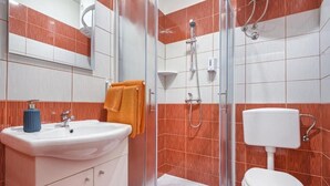 Een badkamer met een wastafel, spiegel, oranje handdoek, douche en toilet.