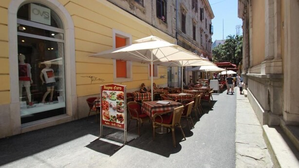 Un café en plein air avec des tables et des chaises, une vitrine avec des mannequins et une enseigne.