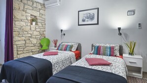 A bedroom with two beds, a stone wall, an air conditioner, a framed picture, and a nightstand with a vase. - Double or twin room  (Pula)