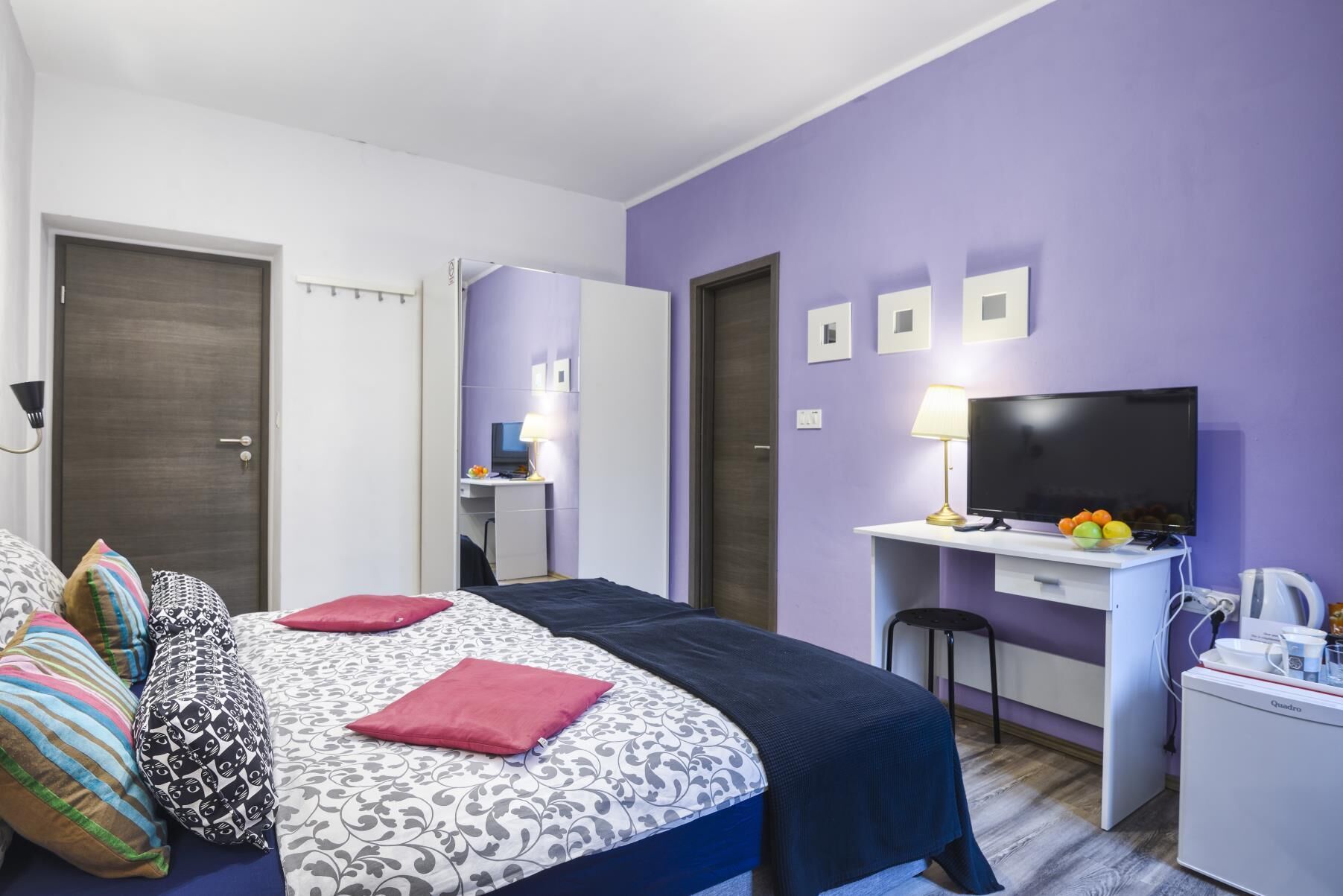 A bedroom with a bed, bedside table, TV, desk, and chair.