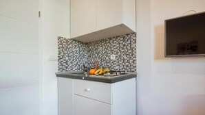 Una cocina compacta con salpicadero de azulejos, estufa empotrada y televisor de pantalla plana montado en la pared.