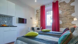Un dormitorio con dos camas, una pared de piedra, un televisor, una mesita pequeña y una ventana con cortinas rojas.