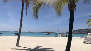 Una playa con palmeras, una orilla arenosa y barcos en el agua.