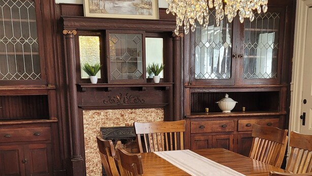 Een eetkamer met een houten tafel, stoelen, een kroonluchter en een kamerbreed tapijt.