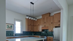 Een moderne keuken met houten kastjes, een groot eiland met barstoelen, een roestvrijstalen koelkast en een backsplash met een herringbone-patroon.