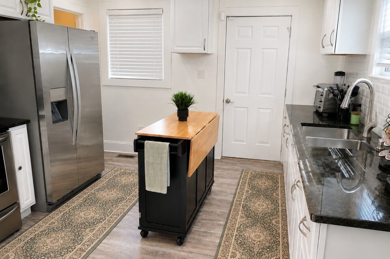 A modern kitchen with a stainless steel refrigerator, a wooden countertop, and a black cart with a towel.