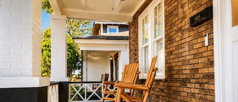 A porch with two rocking chairs, a ceiling fan, and a brick wall with a mailbox.