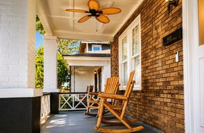 Eine Veranda mit zwei Schaukelstühlen, einem Deckenventilator und einer Ziegelwand mit Briefkasten.