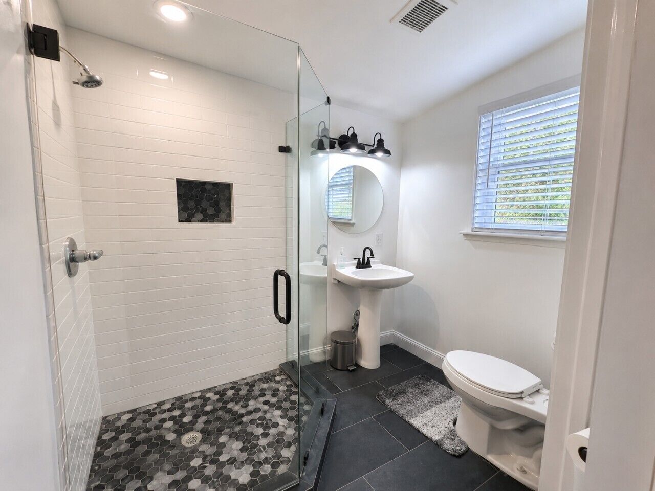 A modern bathroom with a glass-enclosed shower, a white sink, and a toilet.