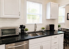 A kitchen with white cabinets, a black countertop, a stainless steel sink, and a toaster oven. - Historic Victorian Restoration (Savannah)