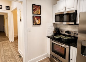 A kitchen with white cabinets, a stainless steel microwave, a stove with pots, and a tiled backsplash.