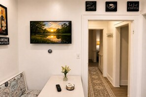 Ein Zimmer mit einem Gemälde von einem Sonnenuntergang über einem See, einer Fernbedienung, einer Vase mit Blumen und einer Wanddekoration mit Kaffeemotiv.