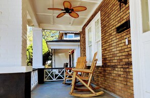 A porch with a rocking chair, a ceiling fan, and a brick wall.