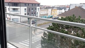 Blick von einem Balkon mit Metallgeländer auf eine Straße mit Gebäuden und parkenden Autos.