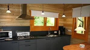 A compact kitchen with wooden walls, a central island, a microwave, a stove, and a sink. - Chalet Copperwing on small-scale nature campsite 't Ol Gat. (Zoutkamp)