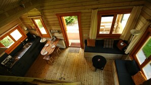 A wooden cabin interior with a dining area, a sofa, and a staircase. - Chalet Copperwing on small-scale nature campsite 't Ol Gat. (Zoutkamp)