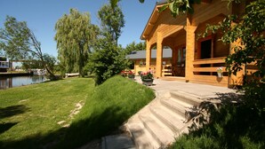 A wooden cabin with a stone staircase leading to a porch, surrounded by a grassy area and trees. - Chalet Copperwing on small-scale nature campsite 't Ol Gat. (Zoutkamp)