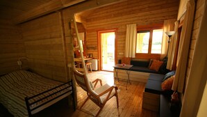 A wooden cabin interior with a bed, a rocking chair, a sofa, and a small table. - Chalet Copperwing on small-scale nature campsite 't Ol Gat. (Zoutkamp)