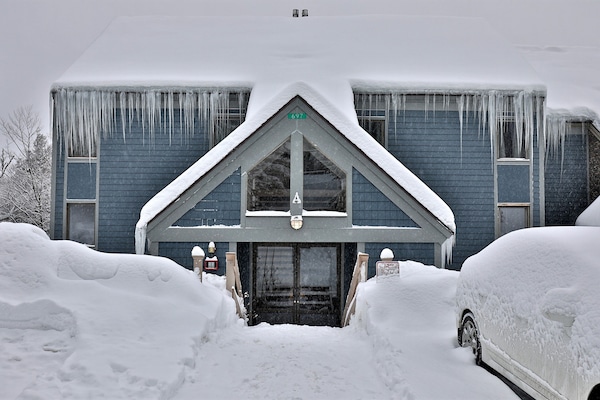 The entry walkway and front door are surrounded by winter snow and nearby parking.