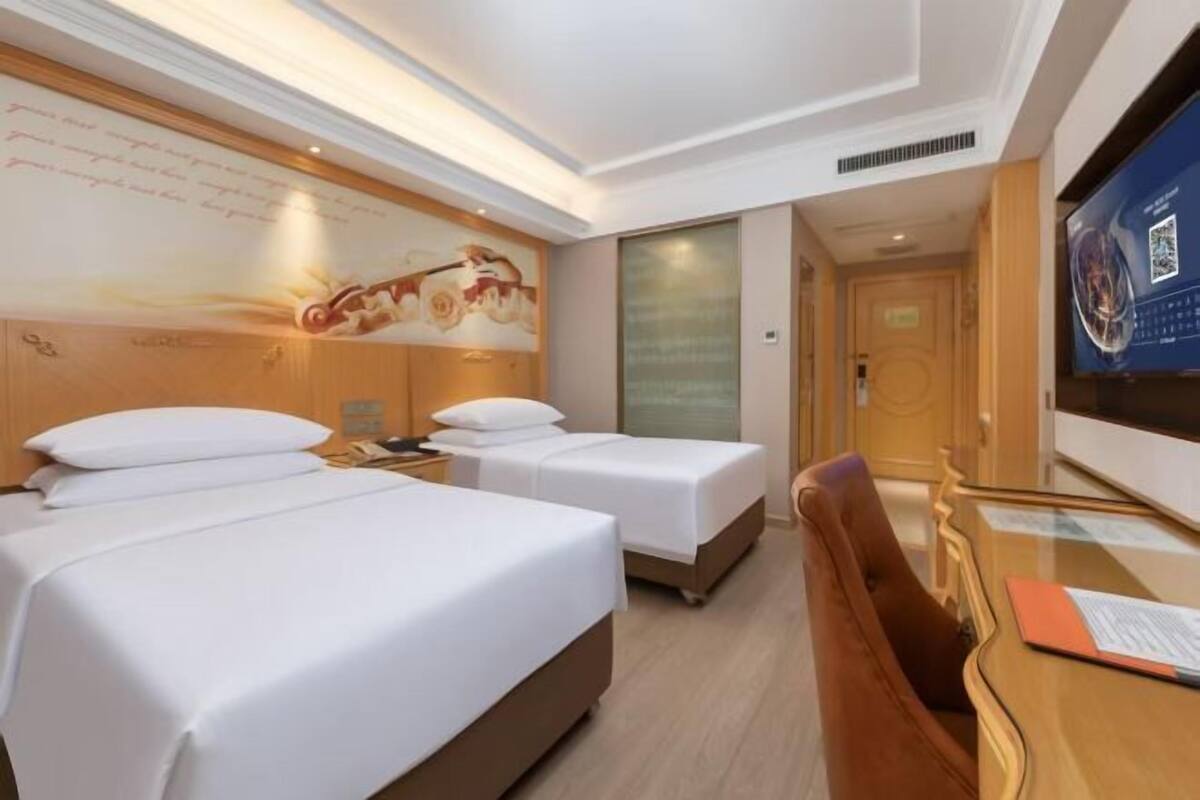 A hotel room with two beds, a desk, a TV, and a mural on the wall.