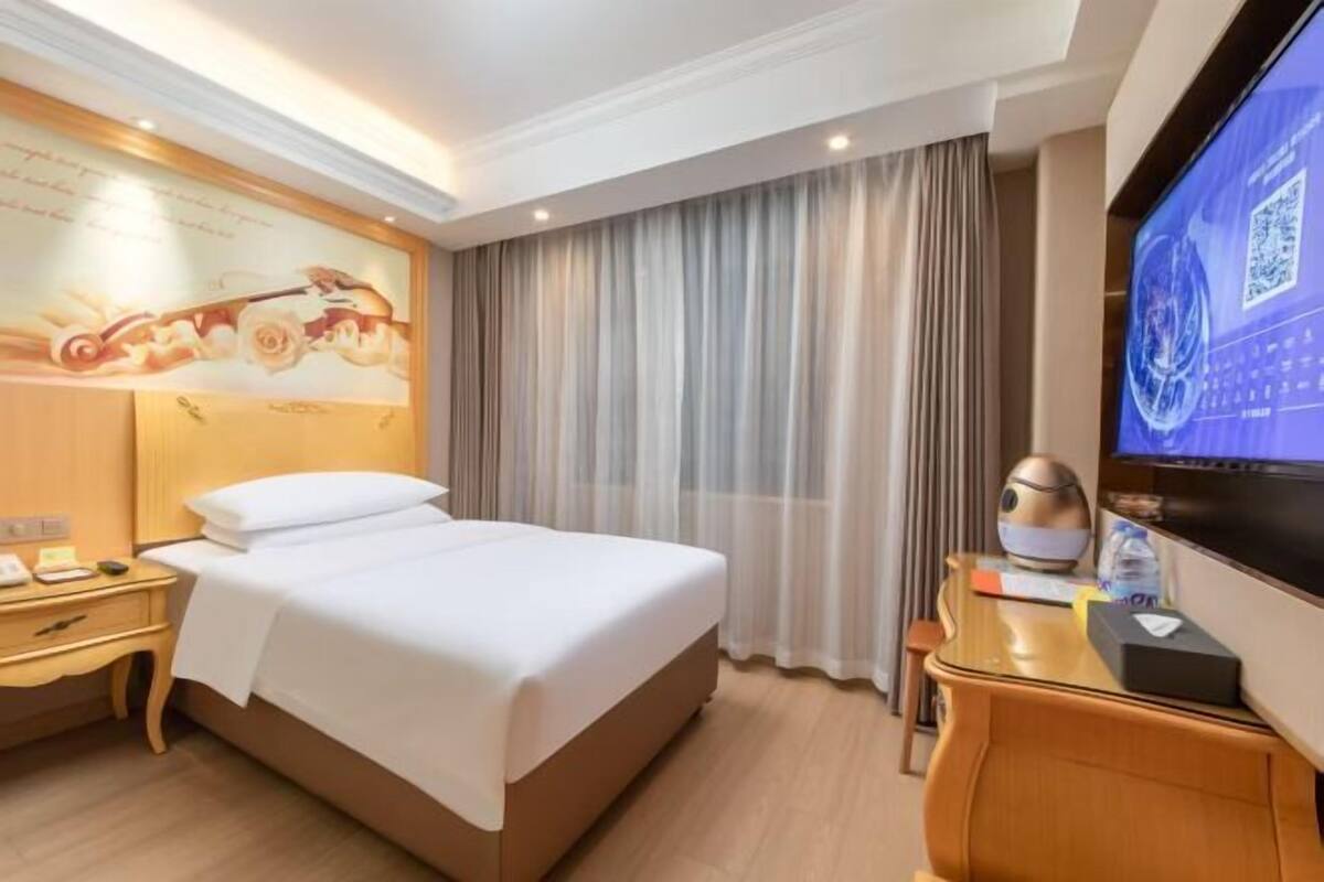 A hotel room with a bed, a desk, a television, and a curtain.